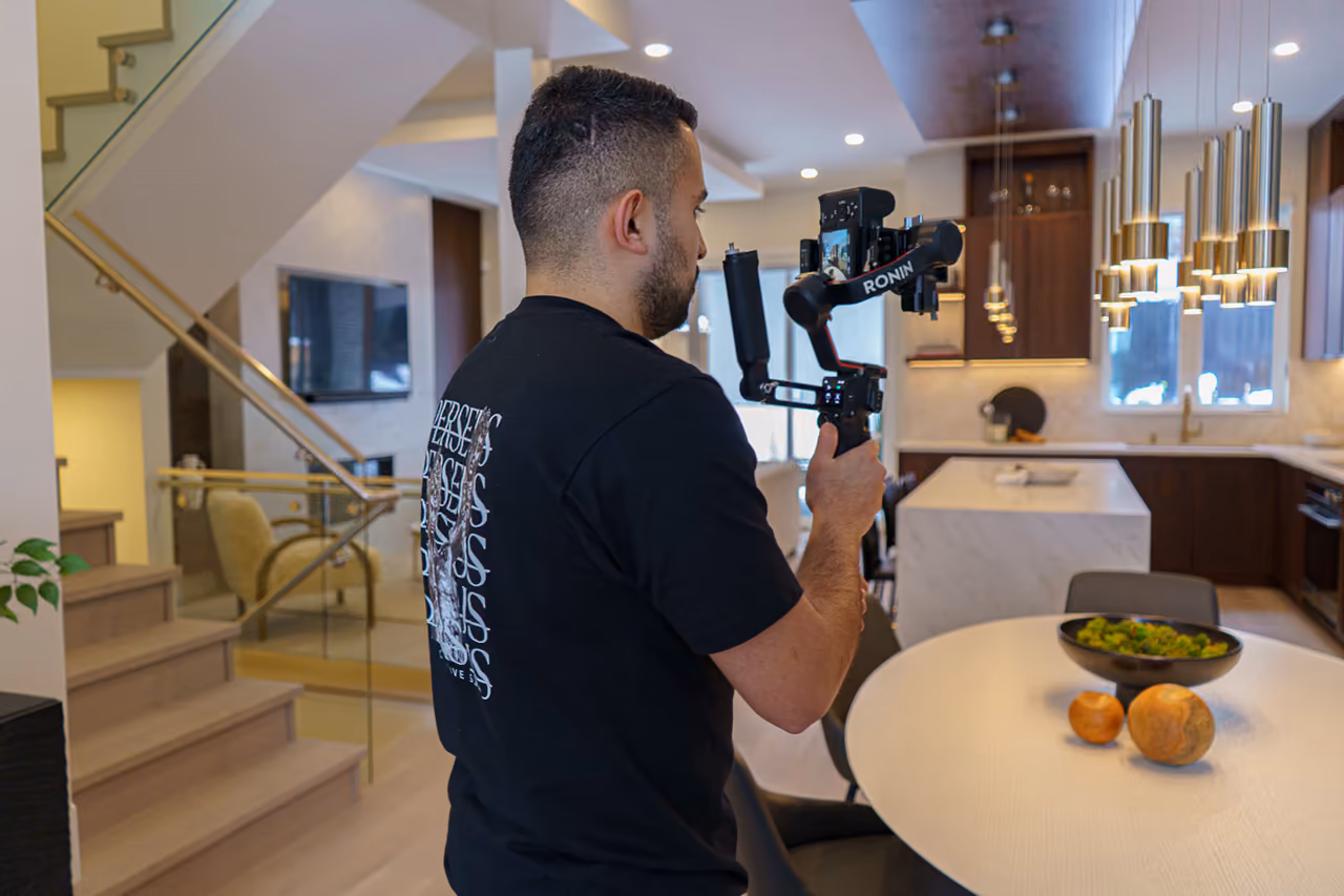 A Perseus Creative Studio videographer films the staircase and foyer of a luxury home, shooting real-estate content with a gimbal-stabilised camera.