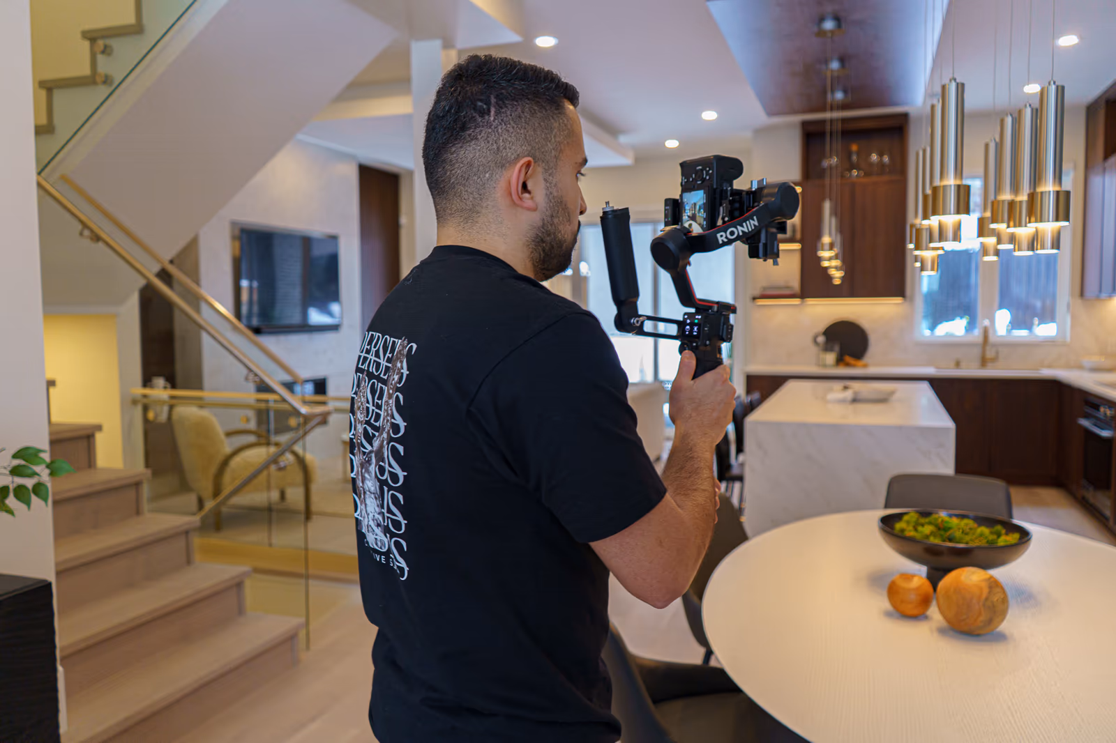 A Perseus Creative Studio videographer films the staircase and foyer of a luxury home, shooting real-estate content with a gimbal-stabilised camera.