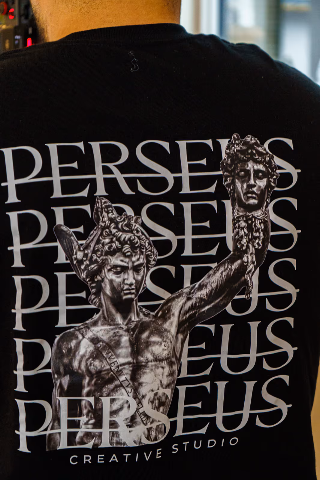 The Perseus Creative Studio Medusa emblem printed across a black t-shirt worn by a crew member — the studio’s founding brand identity.
