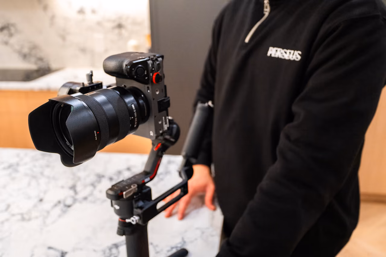 A Perseus Creative Studio videographer holds a gimbal-stabilised Sony camera over a marble countertop, filming the interior of a luxury kitchen.