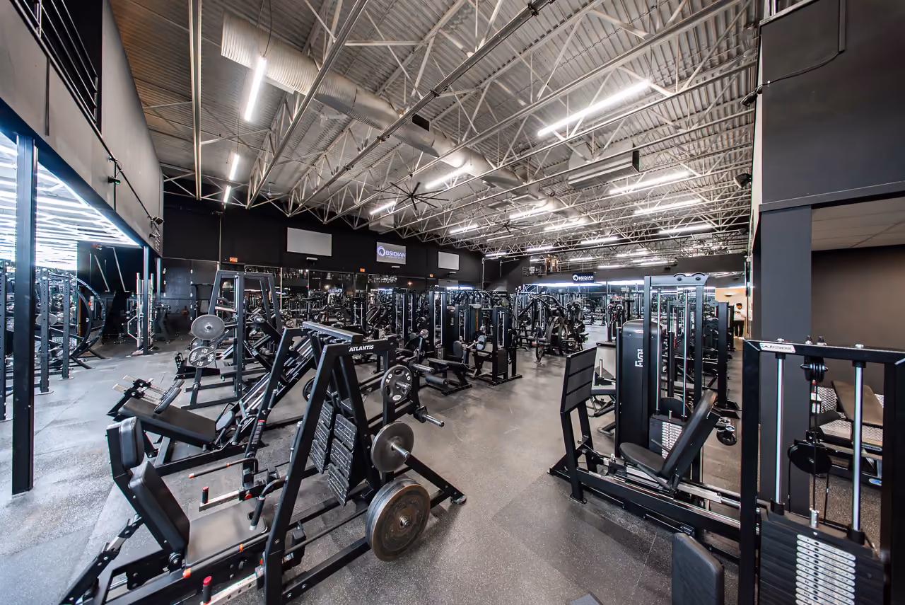 Strength training floor of Obsidian Athletic Club, a North Vancouver gym, with rows of machines under a steel-truss ceiling.