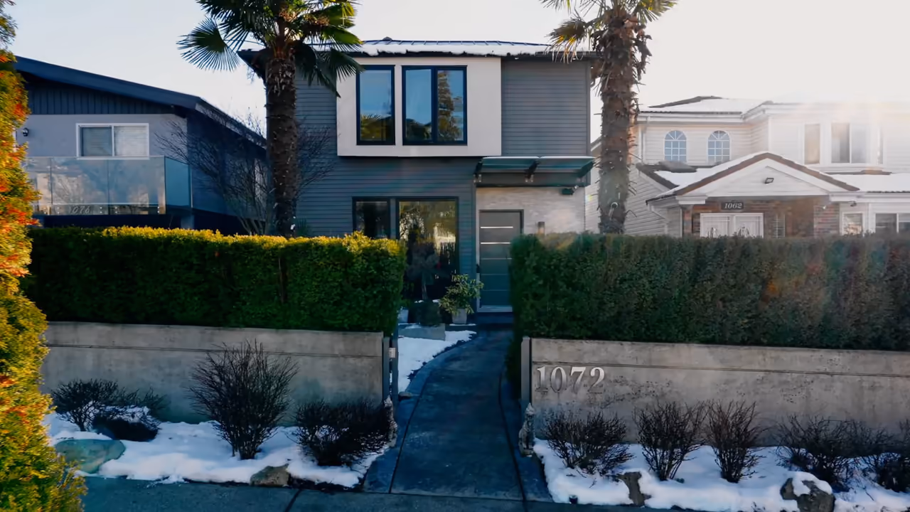 Modern grey two-storey home behind clipped hedges at 1072 E 39th Ave in Vancouver, the street number set into the front wall, captured for Faith Wilson Realty by Perseus Creative Studio.