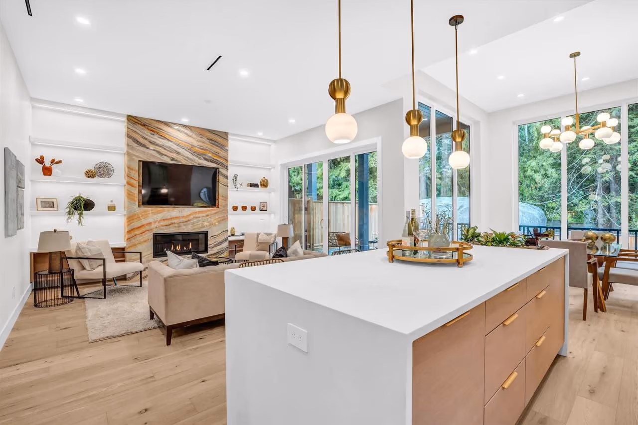 Open-plan kitchen and living room with a waterfall island, brass pendants, and a marble fireplace wall in Vela Homes’ 4442 Hoskins Rd build in North Vancouver, filmed by Perseus Creative Studio.