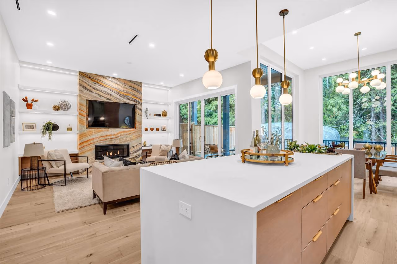 Open-plan kitchen and living room with a waterfall island, brass pendants, and a marble fireplace wall in Vela Homes’ 4442 Hoskins Rd build in North Vancouver, filmed by Perseus Creative Studio.