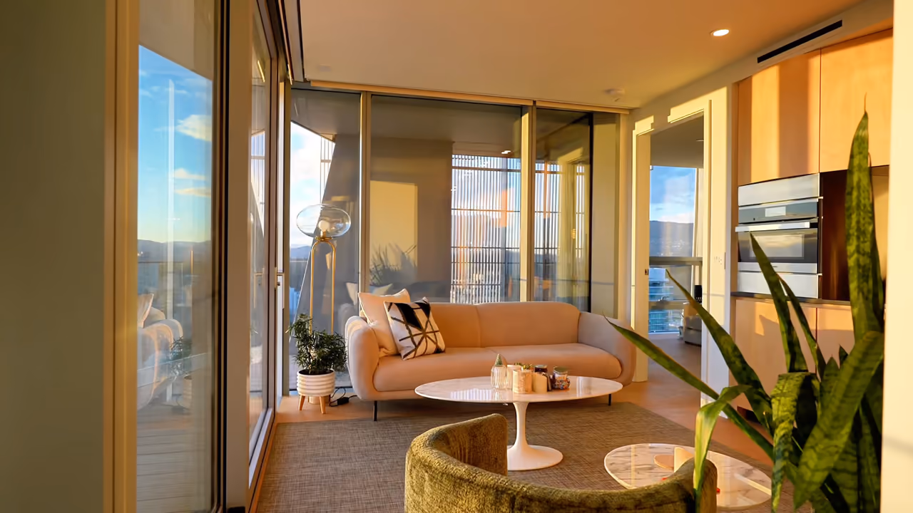Sunlit high-rise living room with curved floor-to-ceiling glass and mountain-and-city views at the Kengo Kuma-designed Alberni tower in Vancouver, filmed for Mana Noori by Perseus Creative Studio.