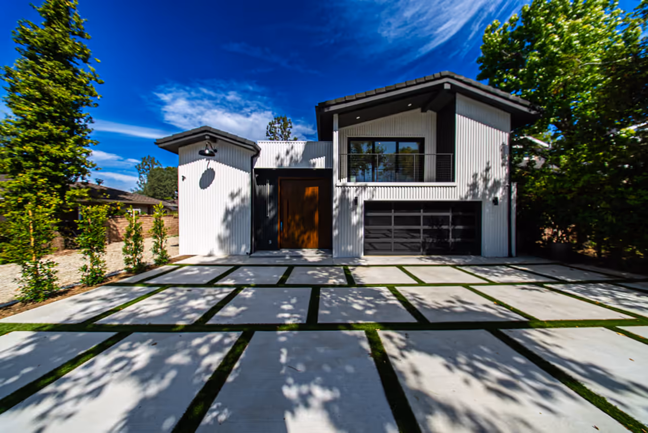 Modern white-and-black custom home with a paver driveway and glass garage door in Encino, Los Angeles, photographed for Encino Development by Perseus Creative Studio.