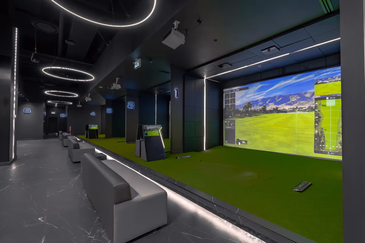 Indoor golf simulator bays with swing screens and lounge seating at Happy Gilmore Golf Lounge, captured by Perseus Creative Studio.