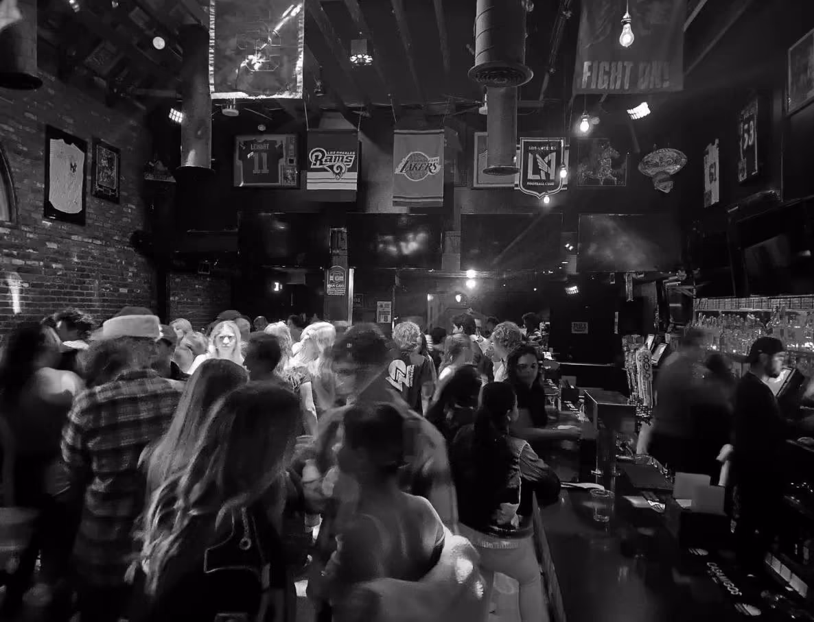 Black-and-white shot of a packed sports-bar crowd beneath team banners during the Howler Head activation at 901 Bar & Grill in Los Angeles, captured by Perseus Creative Studio.