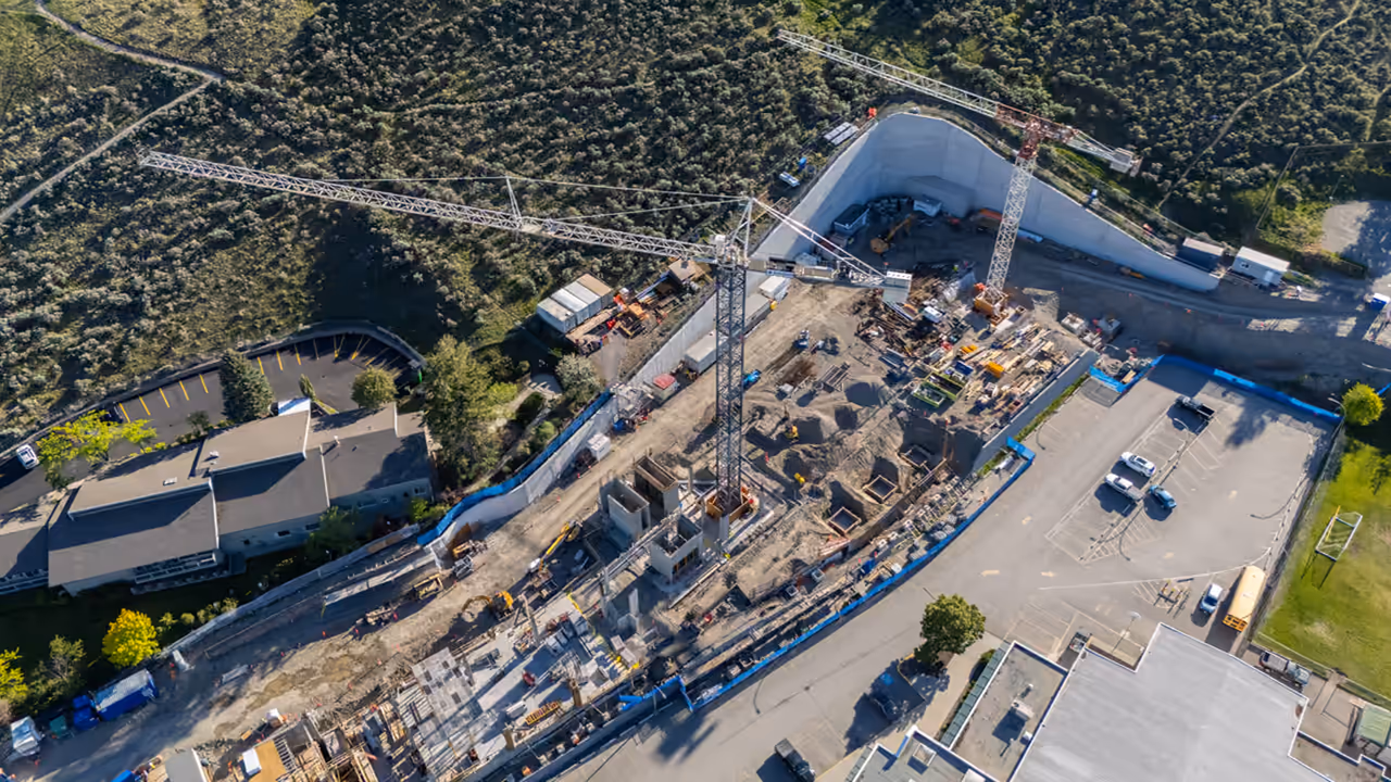 Aerial of the RS Foundation construction site for the Kamloops cancer centre with a tower crane and deep excavation, captured by Perseus Creative Studio.