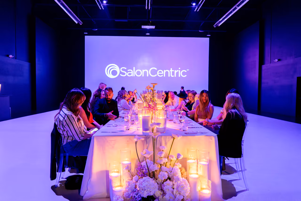 Candlelit appreciation dinner with a projected SalonCentric logo on the wall, event captured by Perseus Creative Studio.